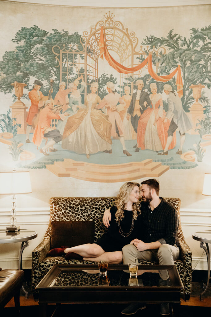 Photo by Pat Cori Photography of a Couple sitting on a sofa together celebrating their engagement.