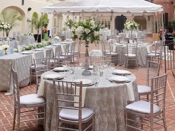 Photo of the Alexandrian wedding reception on the courtyard with canopy with tables adorned with table linens, florals, glass stemware and china. Alexandria Virginia wedding.