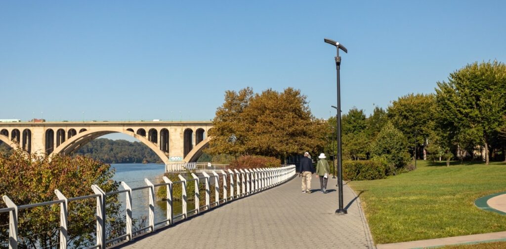 Photo of Georgetown Waterfront Park of the arched bridges and waterfront path with a couple walking for date ideas for Washington DC.