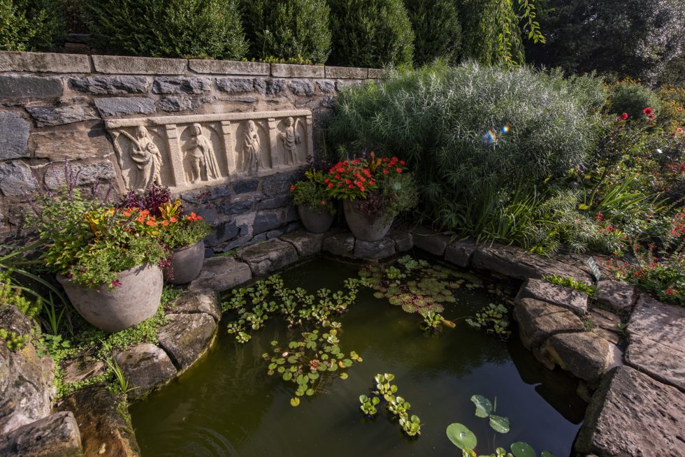 Photo of Bishops Garden fountain surrounded by lush greenery and stone wall. Date ideas for Washington DC