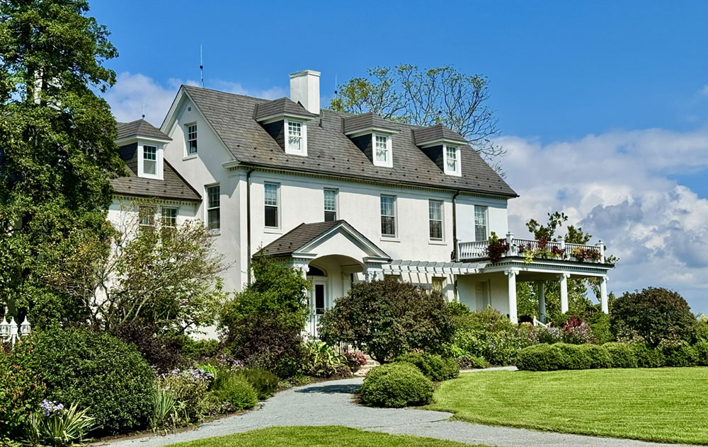 Photo of The River Farm estate with large white stones and a balcony and arbor with lush greenery surrounding the entrance. Alexandria Virginia wedding venue.