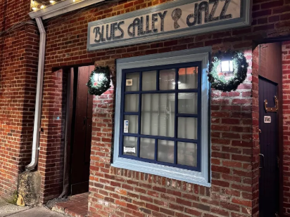 Photo of Blues Alley and Jazz entrance building has red brick entrance and large pane window with garland around the exterior lights. Great things to do in dc is to listen to jazz.