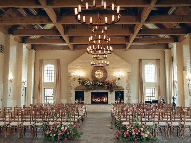 Ceremony area at Early Mountain Vineyards. Rows of chairs with florals flanking the path and the end of room has large brick fireplace with large windows on either side. The wedding venue is in Charlottesville VA.
