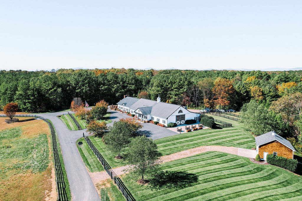 Aerial view of Mount Ida farm and Vineyard. Surrounded by lush woods and manicured grass and wood fence. Farmhouse style estate. A wedding venue in Charlottesville VA.