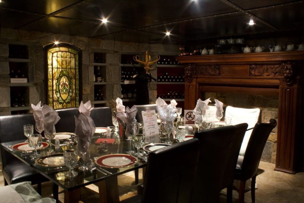 Dining area at the Mansion O Street. Glass table adorned with glass stemware and china. Stain glass and wine bottles and wooden fireplace. Great things to do in DC for an engaged couple.
