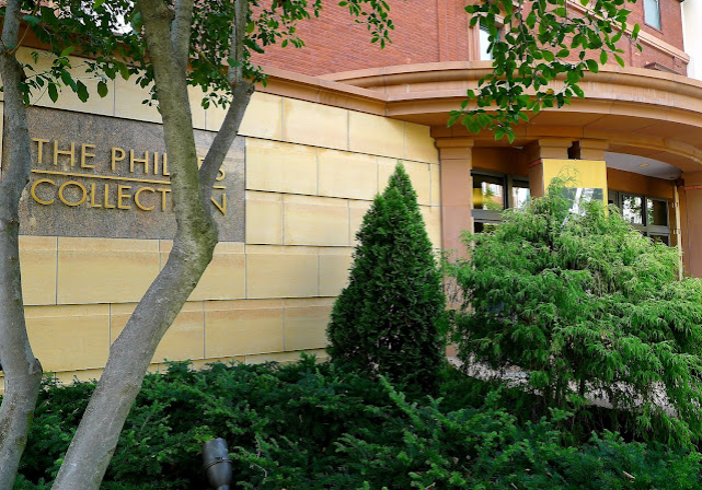 Photo of The Phillips Collection Entrance with stone and brick facade in yellow and red surrounded by lush greenery and trees at the entrance. Great things to do in DC as an engaged couple.