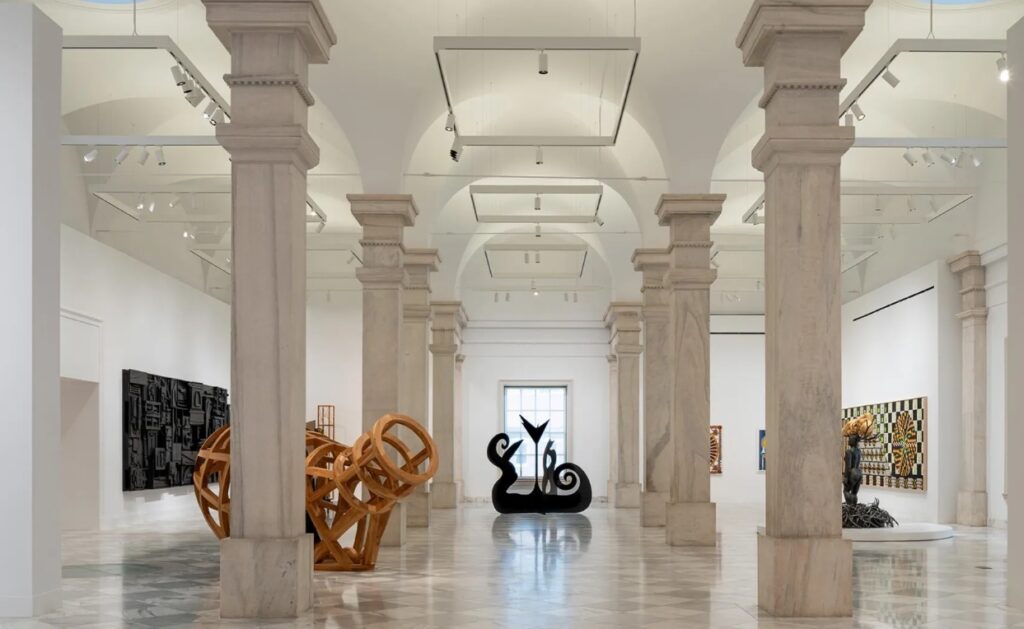 Photo inside The Smithsonian art Museum the interior has large marble columns with a checkered pattern tile floor. Artwork is displayed on the walls and sculptures display on the floor area. Great things to do in DC.