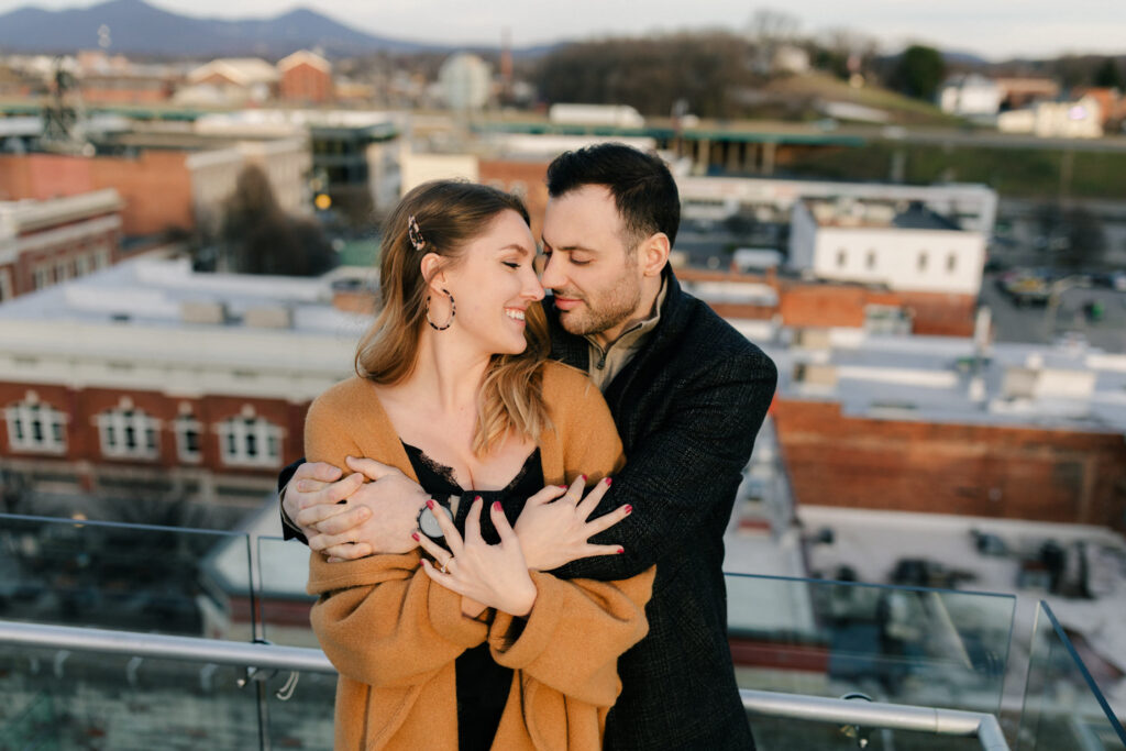 couple hugging on rooftop with roanoke downtown in backgroundengagement photos in roanoke