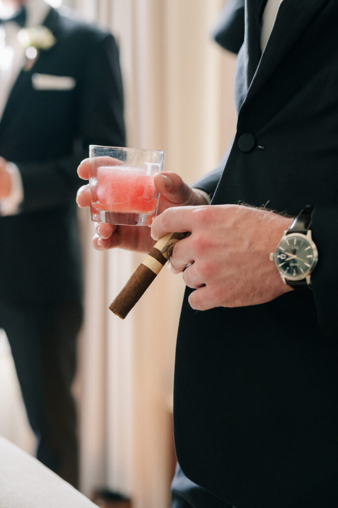 Groom holding cigar and cocktail during black tie wedding getting ready in Lynchburg, VA.