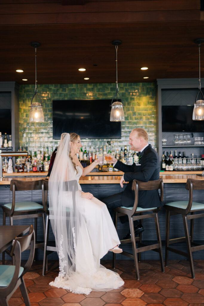 Bride and groom seated at the bar Skyline sharing a toast during black tie wedding portraits at The Virginian Hotel in Lynchburg, VA.