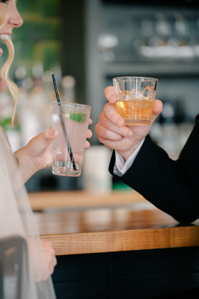 Close-up of bride and groom clinking cocktails during intimate wedding bar portraits at The Skyline at The Virginian Hotel.