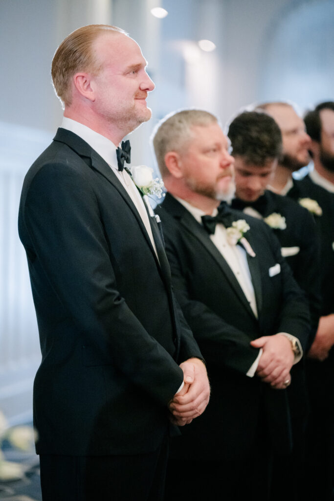 Groom and groomsmen in black tuxedos standing during a wedding ceremony at The Virginian Hotel in Lynchburg, Virginia