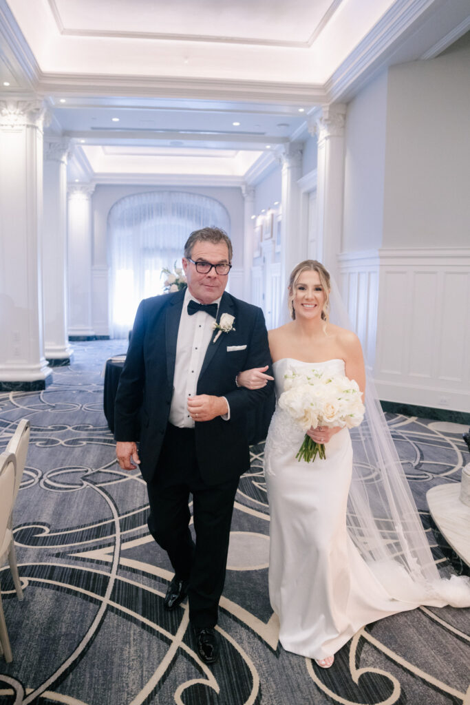 Bride walking arm in arm with her father toward the ceremony inside the elegant ballroom of The Virginian Hotel wedding in Lynchburg