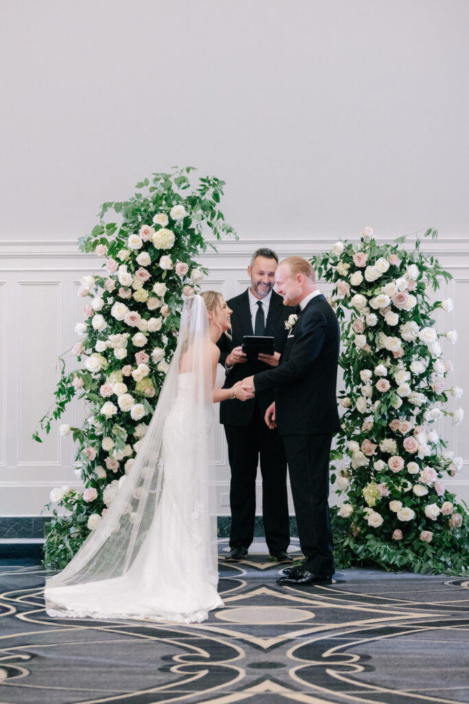Bride and groom exchanging vows beneath floral arches during their ceremony at The Virginian Hotel wedding in Lynchburg