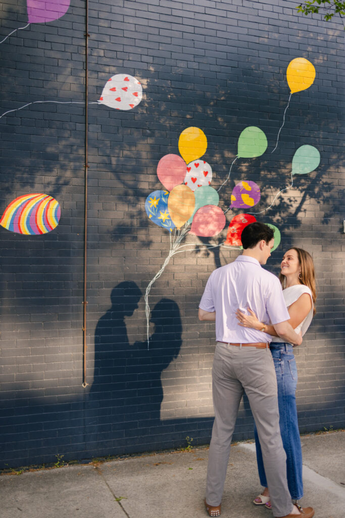 Couple standing in front of colorful balloon mural during playful Downtown Richmond engagement photos
