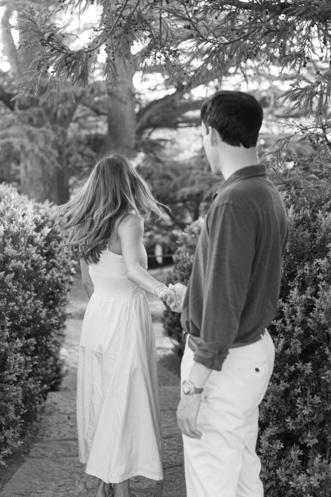 Black and white candid photo of couple walking hand in hand through garden path at Maymont Park