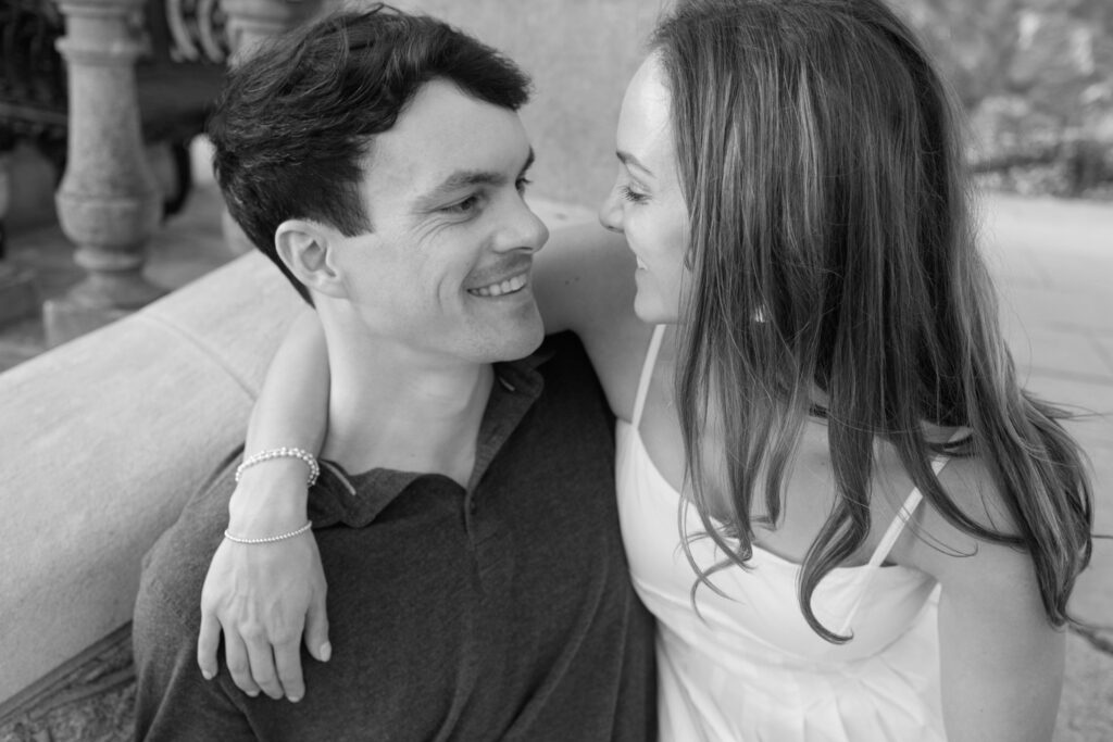 Black and white close-up of engaged couple smiling into each other’s eyes while seated together at Maymont Park in Richmond Virginia