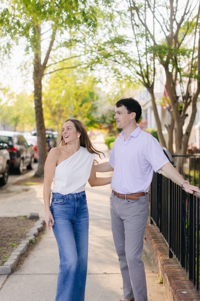 Smiling couple standing beside iron fence on historic Richmond sidewalk during engagement photos.