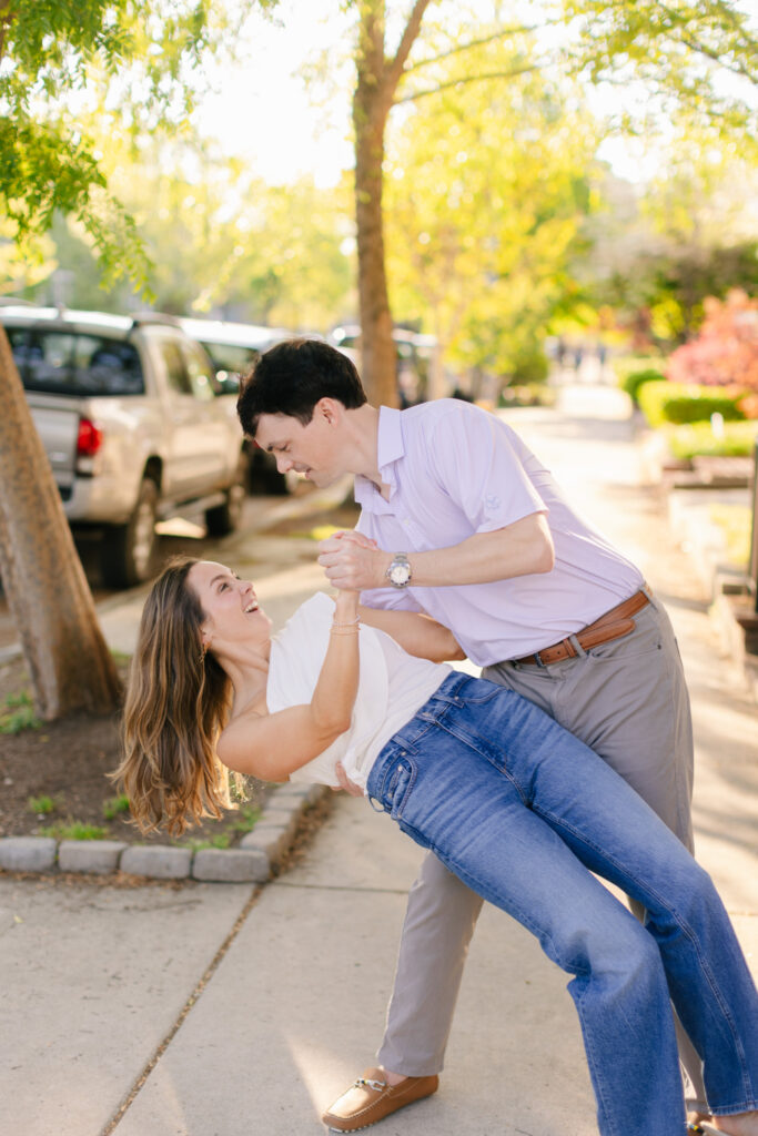 Playful couple laughing as he dips her backward on a sunny Richmond street during engagement session