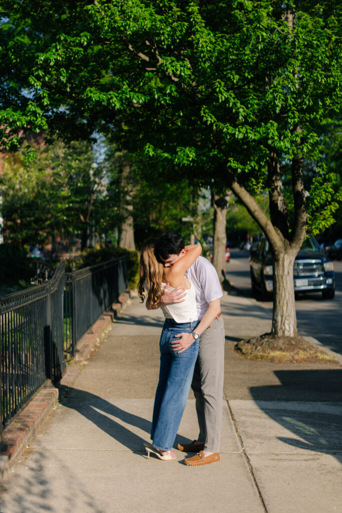 Couple embracing on a tree-lined Richmond sidewalk during golden hour engagement session by Pat Cori Photography.