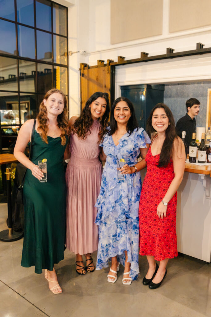 Four wedding guests in colorful dresses posing together during the rehearsal dinner at The Georges in Lexington, Virginia