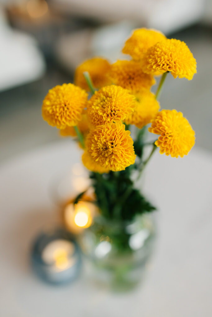 Close-up of bright yellow flowers and candlelight used as simple rehearsal dinner table décor at The Georges in Lexington, Virginia