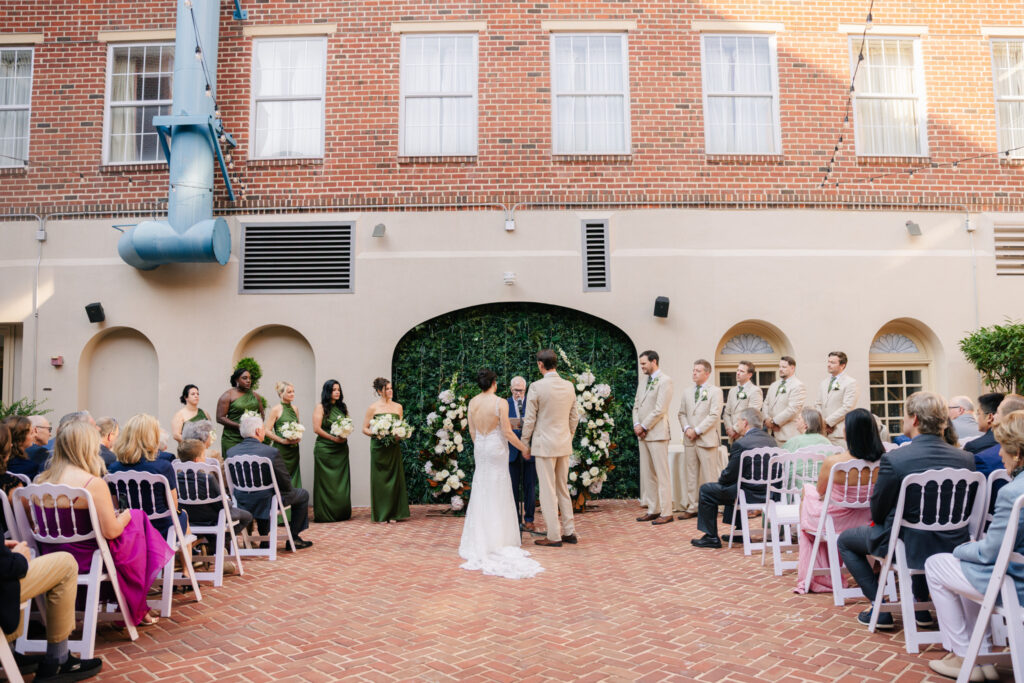 Outdoor wedding ceremony in The Alexandrian Hotel courtyard with bride and groom surrounded by their wedding party and guests
