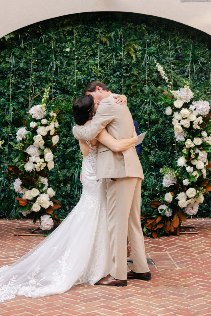 Bride and groom sharing their first kiss during an elegant courtyard wedding ceremony at The Alexandrian Hotel.