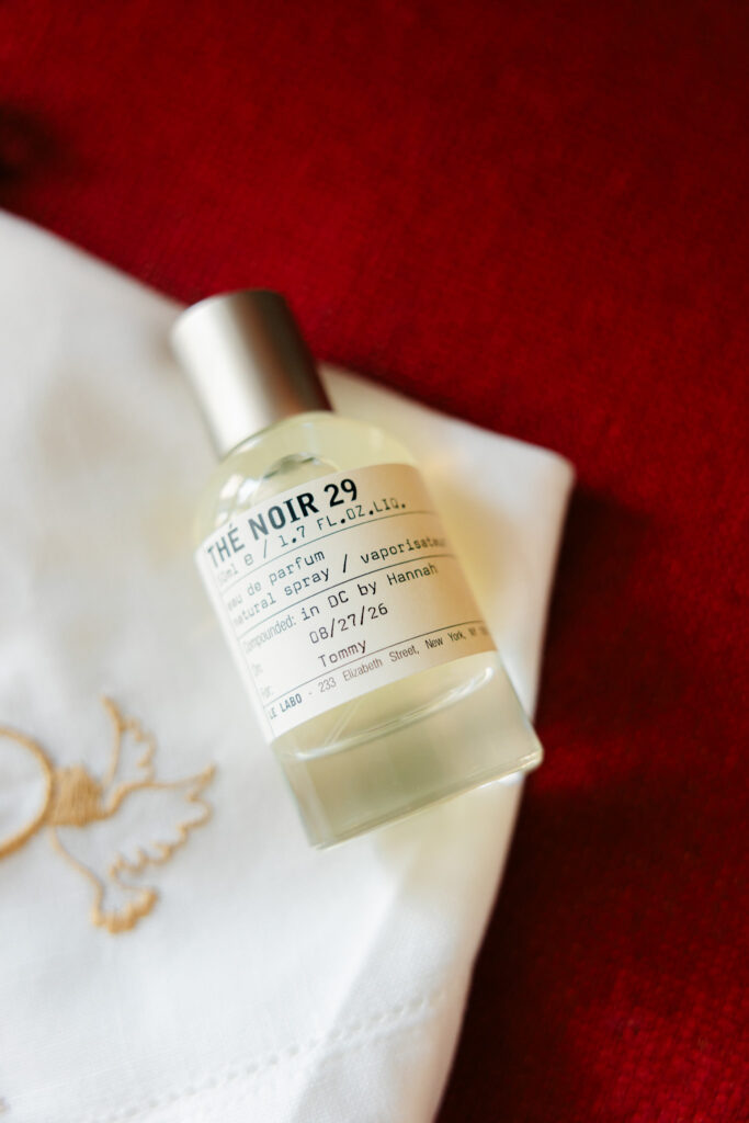 Le Labo Thé Noir 29 fragrance bottle personalized for the groom, styled on white fabric and deep red velvet wedding details