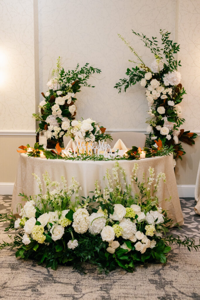 ride and groom sweetheart table surrounded by lush white flowers and greenery at The Alexandrian Hotel wedding reception
