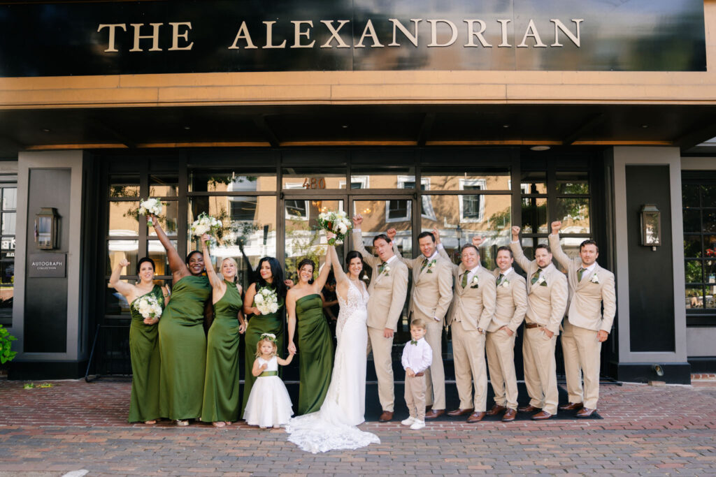 Bride, groom and wedding party celebrating outside The Alexandrian Hotel, with bridesmaids in olive green dresses and groomsmen in neutral suits.
